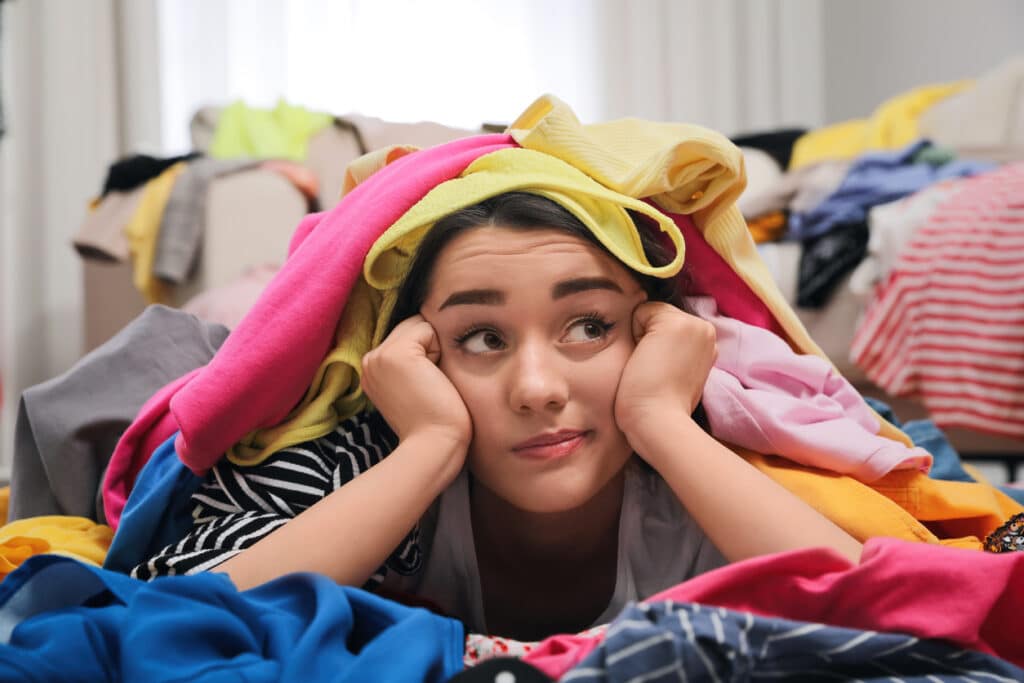jeune femme sous une pile de vêtements